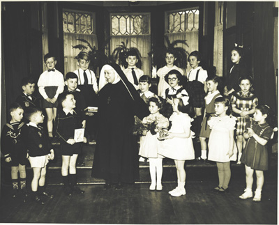 Reproduction d’une photographie des enfants de la maternelle du 360 rue Kenwood, Ottawa (Ontario), avec leur enseignante, soeur Saint-Thomas d’Aquin, ca 1960.