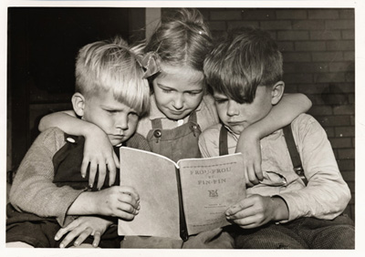 Reproduction d’une photographie de Billy, Rachel et Denny, enfants de M. et Mme William Allen, lisant le manuel d’initiation &agrave; la lecture Frou-Frou et Fin-Fin de Robert Gauthier, septembre 1946.