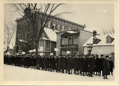 Reproduction d’une photographie d’une manifestation d’&eacute;coliers contre le R&egrave;glement XVII, devant l’&eacute;cole Br&eacute;beuf, square Anglesea dans la basse-ville d’Ottawa (Ontario), &agrave; la fin janvier ou au d&eacute;but f&eacute;vrier 1916.