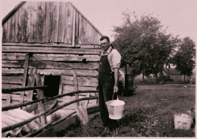 Reproduction d’une photographie de G&eacute;rard Gratton s’appr&ecirc;tant &agrave; nourrir les cochons, Wendover (Ontario), 1945.